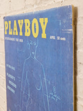 Load image into Gallery viewer, Vintage April 1976 issue of Playboy magazine with a blue cover and yellow logo, leaning against a white brick wall.