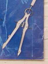Load image into Gallery viewer, A close-up of a vintage-style blue blueprint poster featuring a silver metal compass drawing instrument, with a white brick wall visible on the right side.
