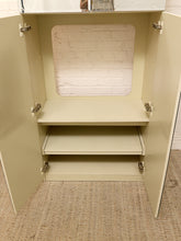 Load image into Gallery viewer, An open cream-colored wooden storage cabinet with two doors swung open, showing two pull-out shelves and a brick-patterned backing panel inside.