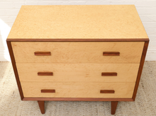 Load image into Gallery viewer, A mid-century modern three-drawer dresser with a light natural burl wood finish and dark brown wood trim and legs, shown on a textured rug against a white brick wall.