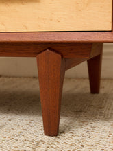 Load image into Gallery viewer, Close-up of a mid-century modern wooden furniture piece, showing a warm reddish-brown wood leg and a light natural wood drawer front, set on a textured beige rug.