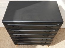 Load image into Gallery viewer, A black six-drawer chest of drawers with a smooth, slightly glossy finish and small wooden feet, photographed from a high angle against a white brick wall and beige rug.