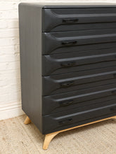 Load image into Gallery viewer, A dark charcoal gray wooden chest of drawers with six curved drawers and light natural wood legs, positioned against a white brick wall on a beige woven rug.