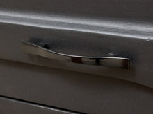 Load image into Gallery viewer, A close-up of a curved, polished chrome metal handle mounted on a dark gray cabinet door.