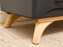 Load image into Gallery viewer, Close-up of a mid-century modern sideboard or cabinet with a dark charcoal gray painted body and light natural wood legs, resting on a woven beige rug.