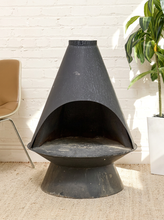 Load image into Gallery viewer, Vintage black metal freestanding fireplace with tall tapered hood, curved asymmetrical opening, circular base, and aged finish