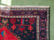 Load image into Gallery viewer, A close-up of a traditional patterned rug corner, showing a dark navy blue field with red, beige, and blue motifs, a cream border, and a red section at the bottom, laid against a green tiled floor.