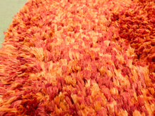 Load image into Gallery viewer, A close-up of a shaggy area rug with a textured, looped pile in warm shades of orange, red, and peach.