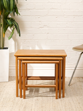 Load image into Gallery viewer, Set of three vintage teak nesting tables in graduated sizes with rectangular tops, rounded edges, slender legs, and warm wood grain