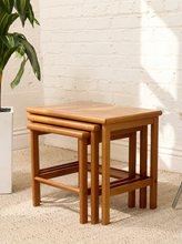 Load image into Gallery viewer, Set of three vintage teak nesting tables in graduated sizes with rectangular tops, rounded edges, slender legs, and warm wood grain