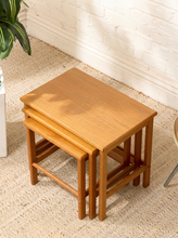 Load image into Gallery viewer, Set of three vintage teak nesting tables in graduated sizes with rectangular tops, rounded edges, slender legs, and warm wood grain