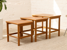 Load image into Gallery viewer, Set of three vintage teak nesting tables in graduated sizes with rectangular tops, rounded edges, slender legs, and warm wood grain