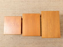 Load image into Gallery viewer, Three square wooden nesting tables or side tables in varying sizes, arranged from smallest to largest on a textured beige woven rug.