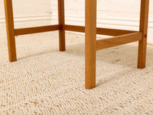 Load image into Gallery viewer, Close-up of a wooden table leg and stretchers on a textured beige woven rug against a white wall.