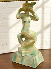 Load image into Gallery viewer, A sculptural decorative figure on a tiered base, painted in distressed turquoise and tan tones, standing on a wooden surface against a white brick wall.