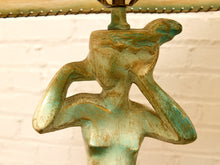 Load image into Gallery viewer, A close-up of a decorative lamp base shaped like a stylized female figure with a distressed turquoise and bronze patina finish, holding a bulb socket at the top against a white brick wall background.