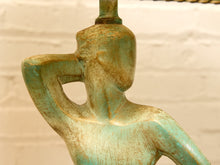 Load image into Gallery viewer, Close-up of a sculptural lampshade or decorative figure with a distressed turquoise and gold patina finish, shown against a light beige brick wall.
