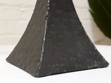 Load image into Gallery viewer, A close-up of a dark charcoal gray textured pyramid-shaped decorative object with a hammered or embossed circular pattern, set against a light off-white brick wall background.