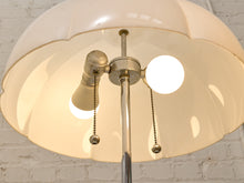 Load image into Gallery viewer, A close-up of a vintage-style floor lamp with a large scalloped off-white glass shade, a central brass pole, and two pull-chain switches, photographed against a white brick wall.