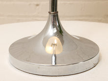Load image into Gallery viewer, A close-up of a polished chrome table lamp base on a white surface with a light brick wall background.