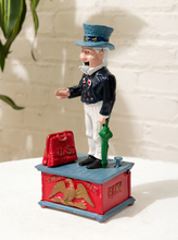 Load image into Gallery viewer, Vintage Uncle Sam figural piggy bank wearing a top hat, dark jacket, bow tie, striped trousers, and standing on a red and blue base