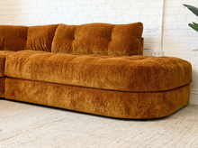 Load image into Gallery viewer, A mid-century modern sectional sofa upholstered in a rich rust-orange velvet fabric, set against a white brick wall and light-colored carpet.