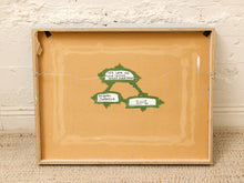Load image into Gallery viewer, A square framed artwork or print with a tan background and a small green hand-drawn diagram in the center containing handwritten notes, leaning against a white brick wall on a beige textured floor.