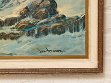 Load image into Gallery viewer, Close-up of a framed landscape painting showing dark rocky cliffs with blue water flowing over them, mounted in a cream and brown frame against a white wall.