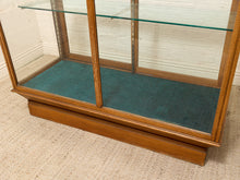 Load image into Gallery viewer, A wooden display case with glass doors and a teal velvet interior, photographed in a room with a light-colored brick wall and textured carpet.