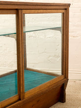 Load image into Gallery viewer, A close-up of a wooden display case with glass doors and shelves, set against a white brick wall and beige carpet.