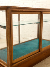 Load image into Gallery viewer, A vintage wooden display case with glass doors and shelves, featuring a teal interior lining, set against a white brick wall.