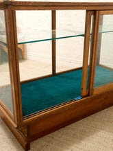 Load image into Gallery viewer, A wooden display case with glass doors and shelves, featuring a teal fabric lining on the bottom, photographed in an indoor setting on a textured carpet.