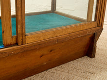 Load image into Gallery viewer, Close-up of a vintage wooden display case or cabinet with glass panels, showing a teal interior lining and a weathered brown wood base on a textured beige carpet.
