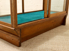 Load image into Gallery viewer, Close-up of a vintage wooden display case or cabinet with glass panels and a teal interior lining, resting on a beige textured rug.