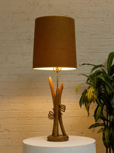 Load image into Gallery viewer, Vintage table lamp with sculptural curved wood base and tall brown woven-texture shade illuminated with a warm glow