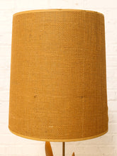 Load image into Gallery viewer, A cylindrical lampshade made of textured natural burlap or jute fabric in a warm tan-brown color, shown against a white painted brick wall background.