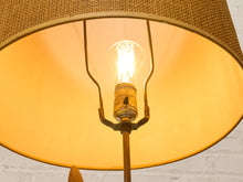 Load image into Gallery viewer, A close-up of a vintage-style table lamp featuring a large warm yellow-golden drum shade, a brass metal fixture, and a glowing light bulb.