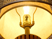 Load image into Gallery viewer, Close-up of a vintage-style table lamp with a glowing warm yellow bulb, brass-toned metal socket, and a dark woven lampshade.