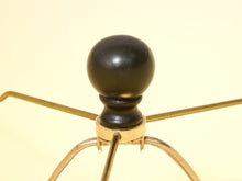 Load image into Gallery viewer, Close-up of a black spherical finial on a brass five-arm stand against a pale yellow background.