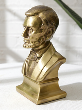 Load image into Gallery viewer, A metallic gold/brass bust sculpture of Abraham Lincoln in profile, standing on a matching rectangular base against a white textured background with soft shadows.