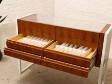 Load image into Gallery viewer, A mid-century modern wooden organizer cabinet with a glass top and multiple pull-out drawers containing white divider inserts, set against a white brick wall and beige carpet.