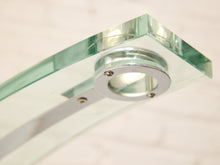 Load image into Gallery viewer, Close-up of a modern glass shelf or tabletop mount with a polished silver circular bracket and clear glass panels on a light marble background.