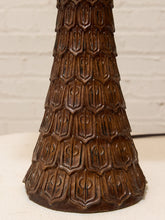 Load image into Gallery viewer, A close-up of a dark brown carved wooden object with a repeating geometric pattern, standing against a white brick wall background.