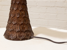 Load image into Gallery viewer, Close-up of a dark brown textured table lamp base with a sculpted geometric pattern, showing the power cord extending to the right against a white brick wall background.