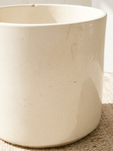 Load image into Gallery viewer, A close-up of a large, cylindrical ceramic planter pot in a warm cream or off-white glaze, resting on a woven natural fiber mat.