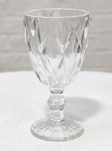 Load image into Gallery viewer, A clear cut-glass goblet with a diamond-patterned bowl and a flared base, photographed on a white textured surface against a light gray background.