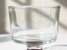 Load image into Gallery viewer, A clear glass pedestal bowl or cup with a thick base, photographed on a white surface with soft natural shadows in the background.