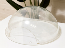 Load image into Gallery viewer, A clear, dome-shaped plastic cover with a semi-circular base, shown on a white surface with a blurred indoor background.