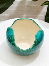 Load image into Gallery viewer, A handmade ceramic bowl with a glossy teal and green marbled exterior and a warm cream-colored glazed interior, resting on a white textured surface.