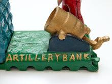 Load image into Gallery viewer, Close-up of a green cast iron artillery bank featuring a gold cannon and a red cannonball, with 'ARTILLERY BANK' embossed in gold on the front, set against a plain white background.